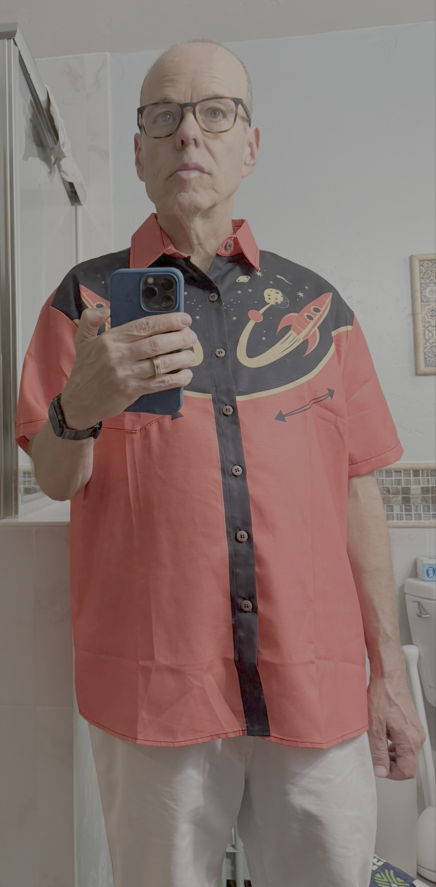 Bathroom selfie in a full-length mirror of a man wearing a red and black retro bowling-style shirt with rocket ships, planets and stars printed across the chest.